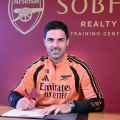 Mikel Arteta smiles while holding his new Arsenal contract at the Emirates Stadium, celebrating his long-term commitment following the team's historic Premier League title win. (Photo: Football news)