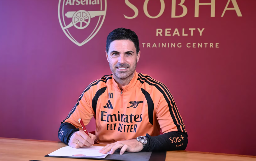 Mikel Arteta smiles while holding his new Arsenal contract at the Emirates Stadium, celebrating his long-term commitment following the team's historic Premier League title win. (Photo: Football news)